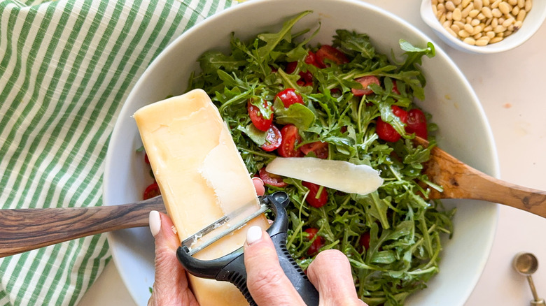 hands adding shaved parmesan to salad