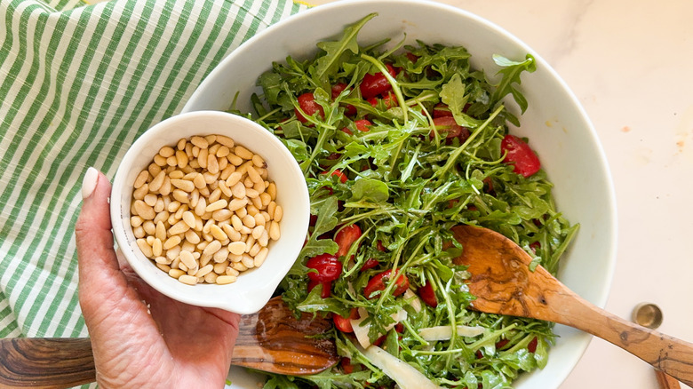 hand adding pine nuts to arugula salad