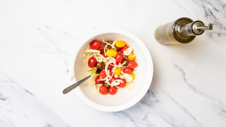 Seasoned cherry tomatoes and onion in bowl.