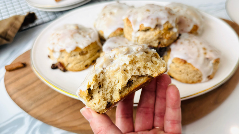 Hand holding cinnamon raisin biscuit in front of platter of biscuits