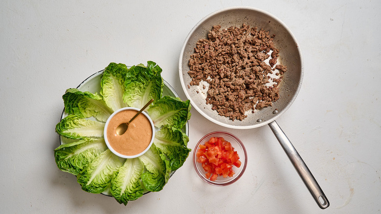 lettuce wraps on a table with sauce in a bowl and beef in a skillet