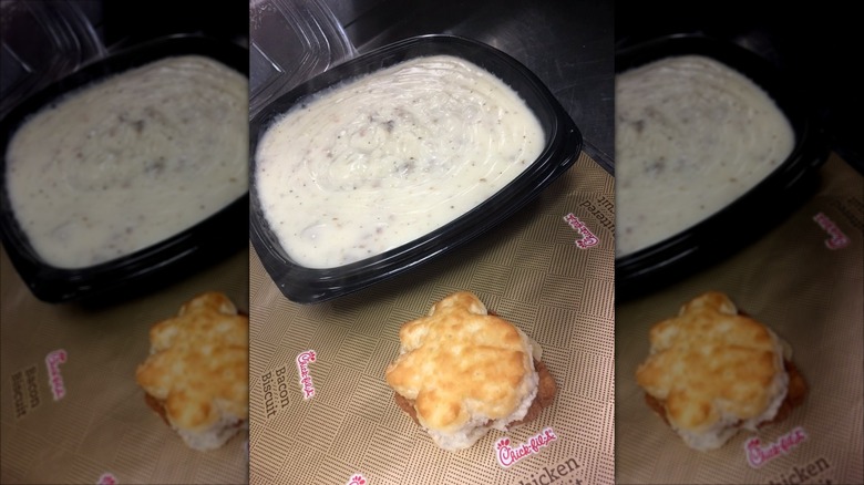 Large black container of sausage gravy next to a small chicken biscuit