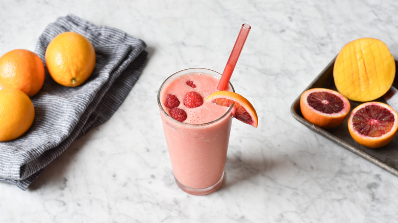 Blood orange smoothie garnished with orange wedge and raspberries
