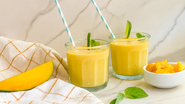 Mango smoothies with straws, mint, and lime wedges