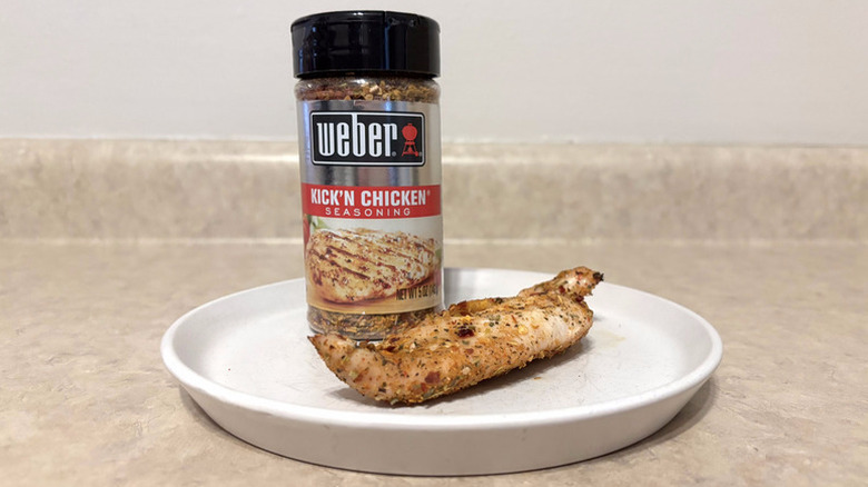 Jar of Weber Kick'N Chicken Seasoning on plate next to piece of cooked, seasoned chicken