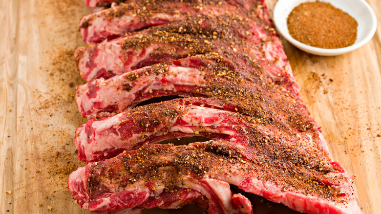 Beef ribs coated with dry rub on wooden board