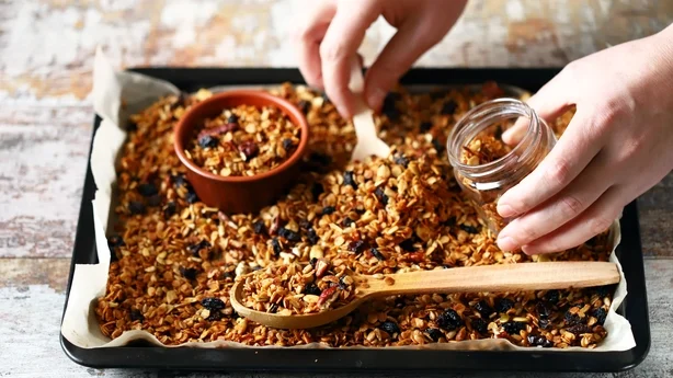 Freshly made homemade granola on a baking sheet. Granola in a wooden spoon and in a jar. Selective focus. Healthy diet concept. Keto diet.