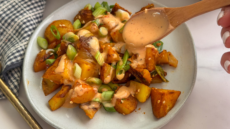 spoon adding sauce to potatoes