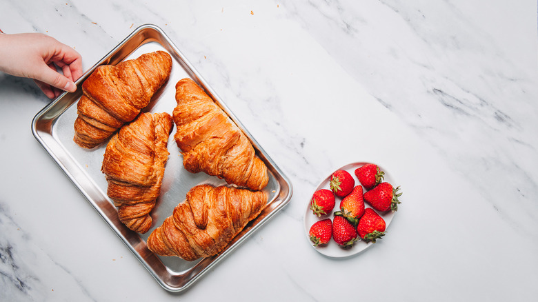 Four croissants on metal sheet beside strawberries.