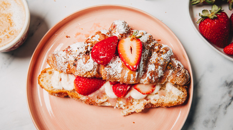 Strawberry cheesecake croissant on a pink plate beside a coffee.