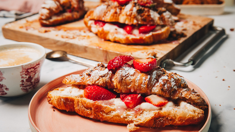 A strawberry cheesecake croissant on a plate beside more on a cutting board in background.