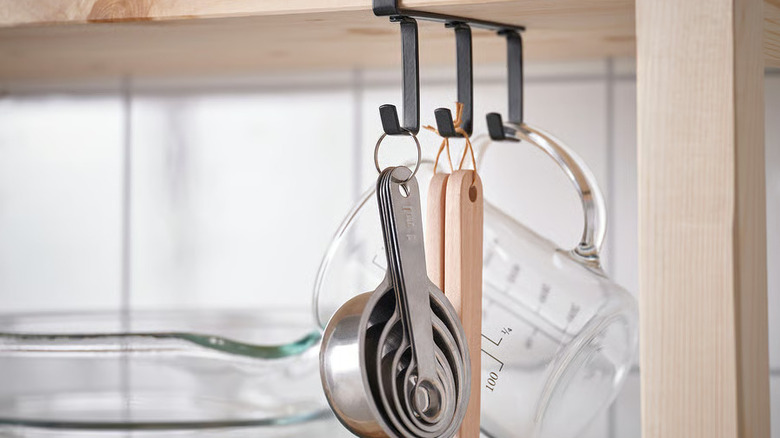 Measuring cups and utensils hanging from hooks under shelf