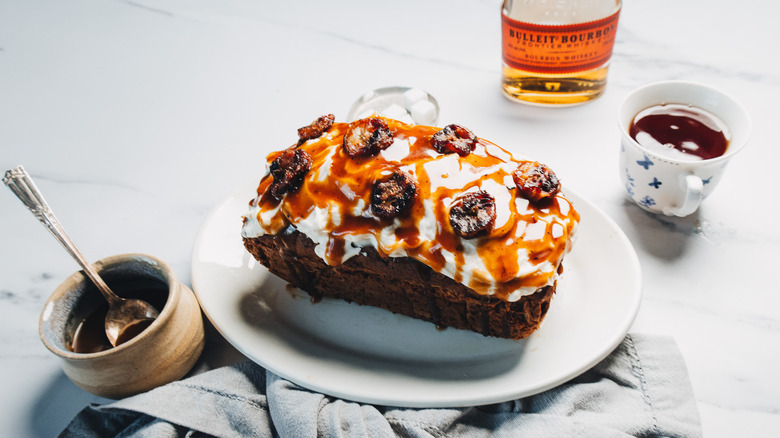 Bourbon banana bread on platter with banana slices, bourbon sauce, tea, and a bourbon bottle.