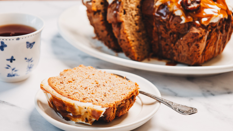 Banana bread slice on a plate with banana bread in background.