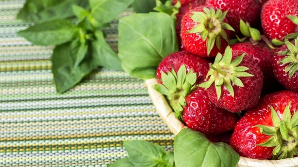 Ripe sweet strawberries in wicker basket and mint leaves on wooden background