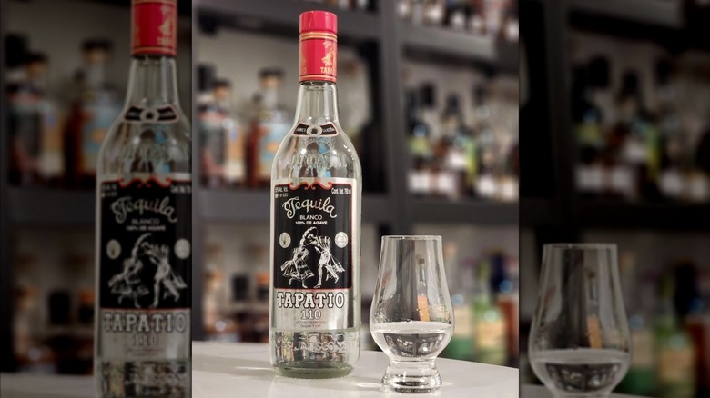 Bottle of Tapatio 110 set on a table alongside short snifter glass with clear spirit