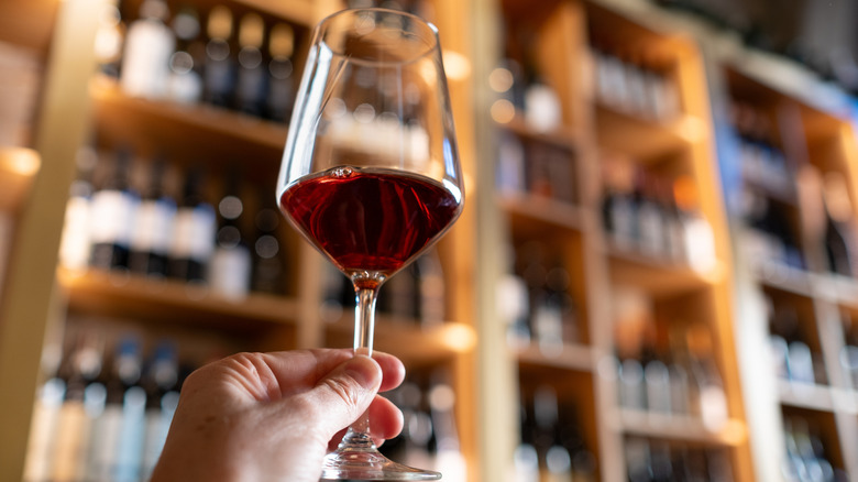 Hand holding a glass of red wine in a wine shop
