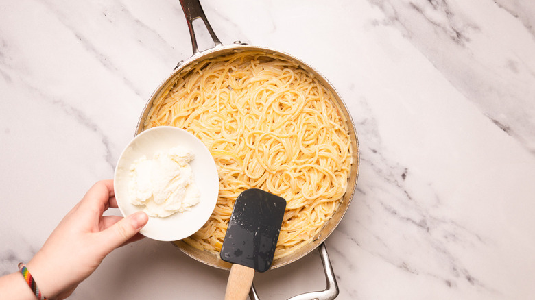 Adding ricotta to creamy sauce.