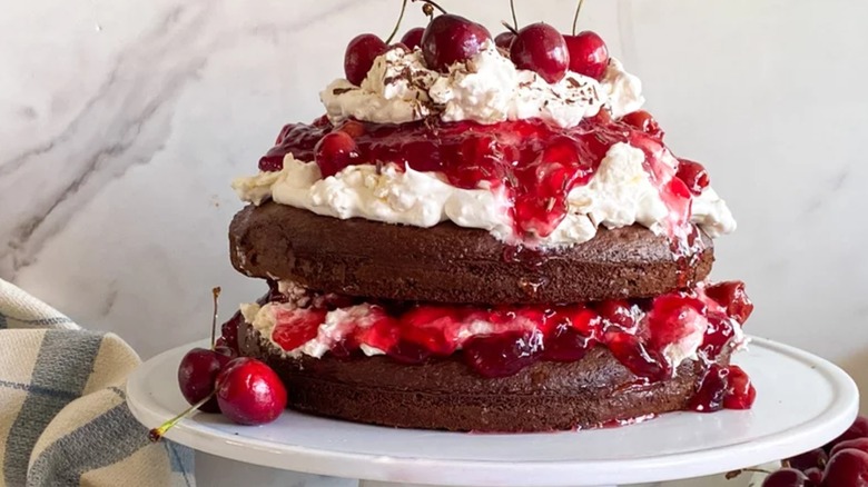 Black forest cake piled with cream and cherries on white cake stand