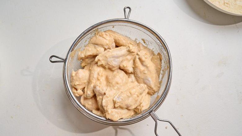 chicken in a colander over marinade in a bowl