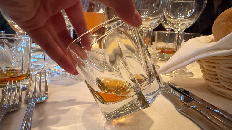 Hand holding tilted glass of Stetson Bourbon on dining table, glasses in background