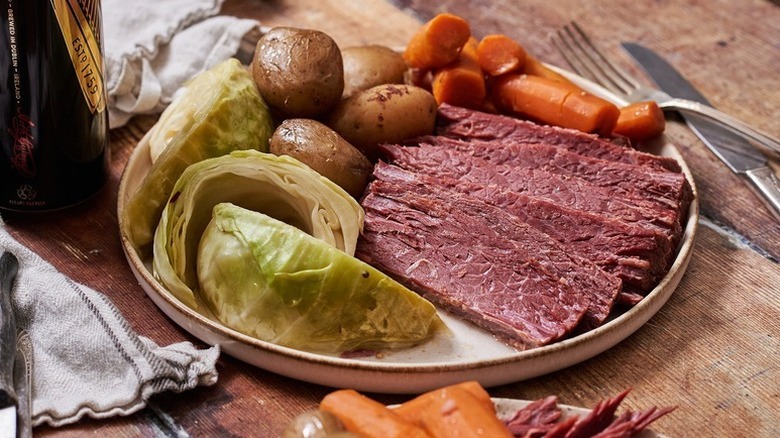 Corned beef slices on a plate with cabbage wedges, baby potatoes, and carrots