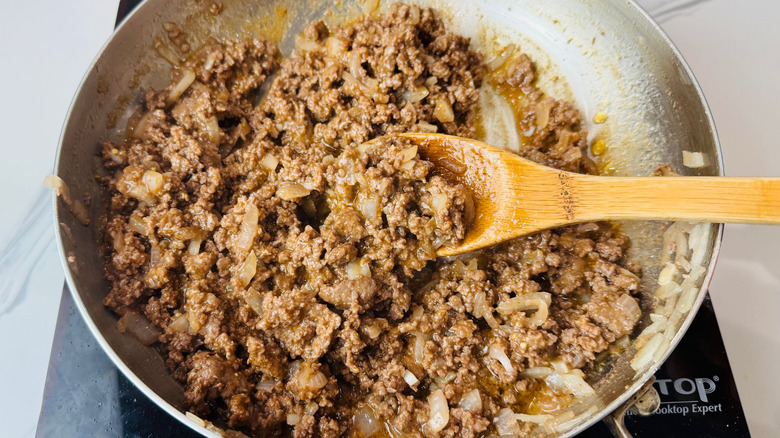 Wooden spoon stirring beef mixture in skillet