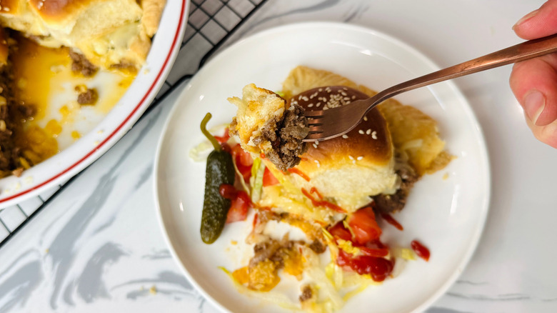 Fork holding bite of cheeseburger pie over slice on plate