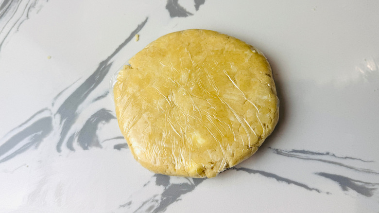 Plastic wrapped dough disc on countertop