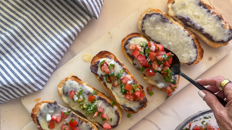 hand spooning pico de gallo onto mollete