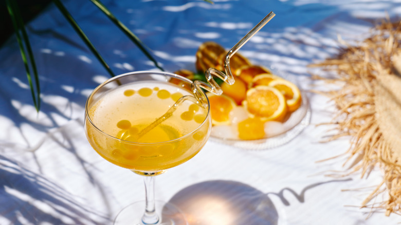 A spiked orange lemonade cocktail in a coupe on an outdoor table.