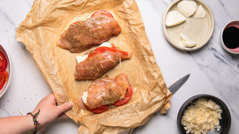 Hand holding baking sheet with three raw Caprese-stuffed chicken breasts