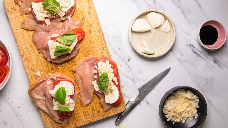 Four raw Caprese-stuffed chicken breasts on cutting board