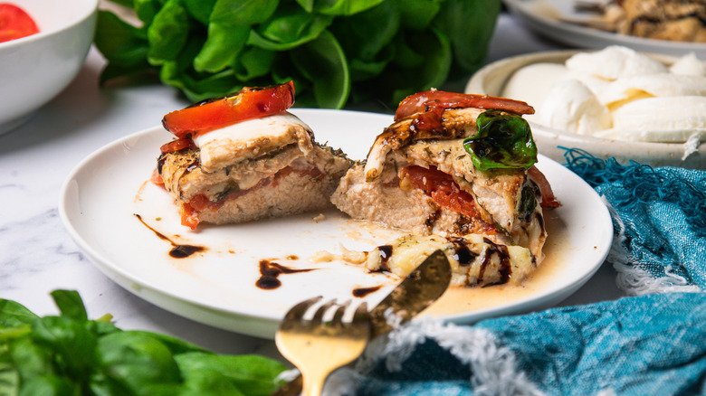 A Caprese-stuffed chicken breast, cut in half, on a white plate