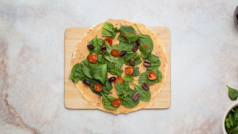 Spinach, olives, tomatoes, and basil on hummus-coated tortilla
