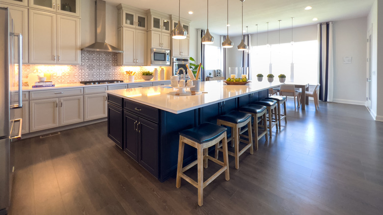 A large, modern kitchen, with cabinetry in white and an oversized and dark contrasting island, in a home with a wide-open floor plan