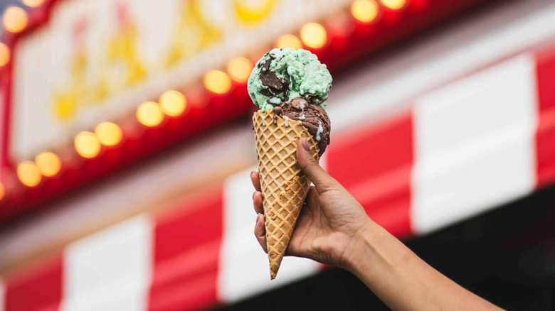 Hand holding up an ice cream cone with neon sign in the background