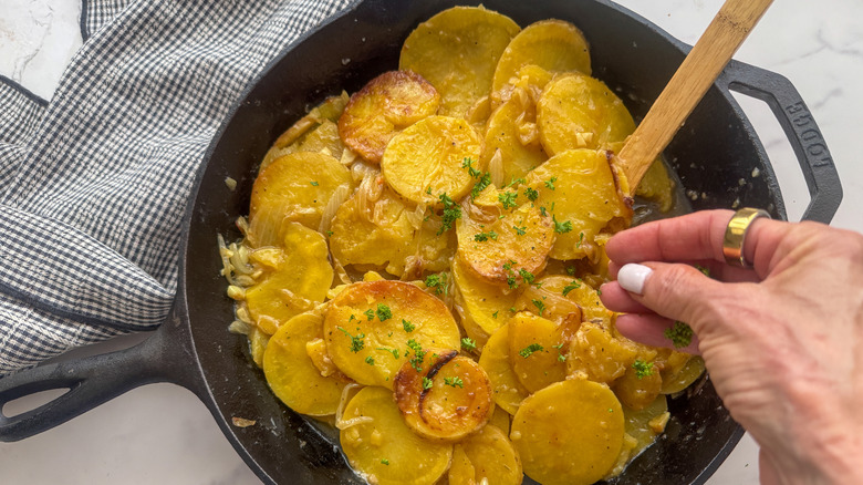 hand adding parsley to potatoes in skillet