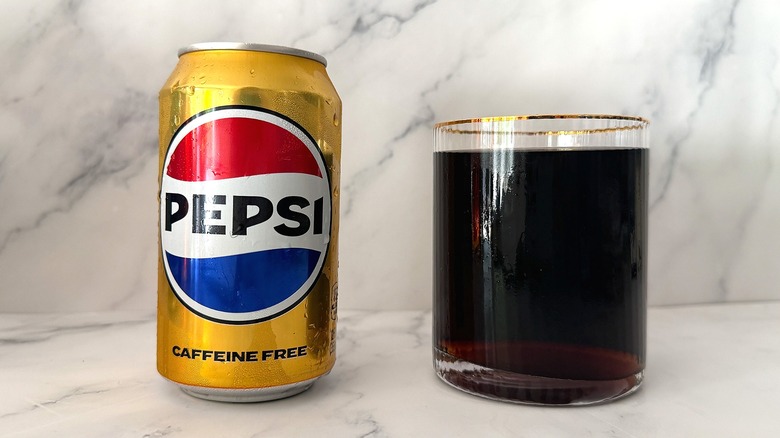 Can of Caffeine Free Pepsi next to gold-rimmed glass of Pepsi on marble surface