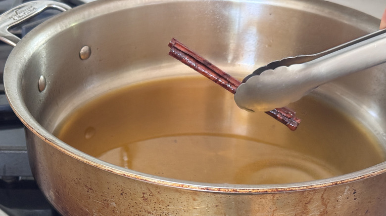 tongs holding cinnamon sticks above pan