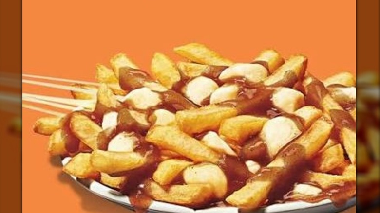 A plate of poutine with a cheese pull coming of the left side