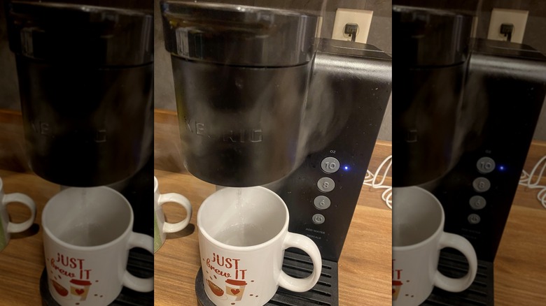 Mirrored image of smoking Keurig coffee machine pouring water into mug