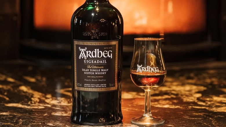 A bottle of Ardbeg Uigeadail in front of a fiery blurred background and next to a filled glass