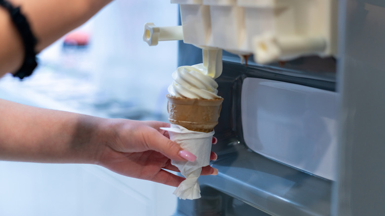 Person dispensing vanilla soft serve ice cream into a cake cone