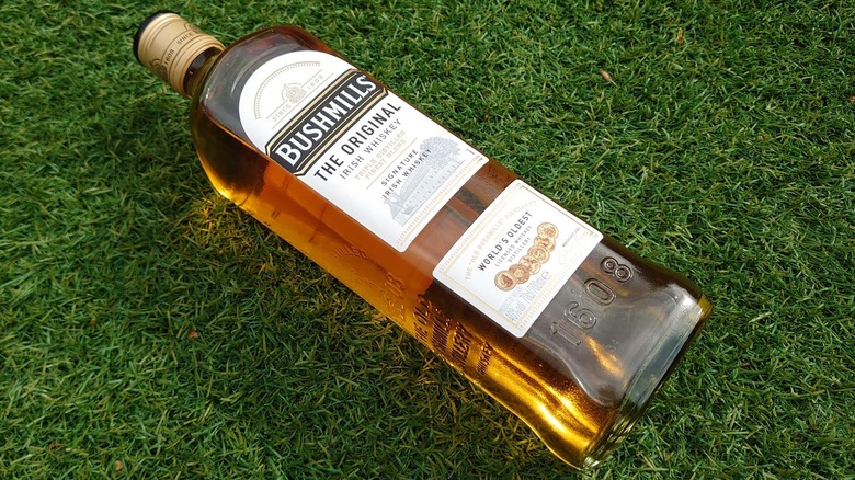 A bottle of Bushmills Original placed down diagonally on artificial grass