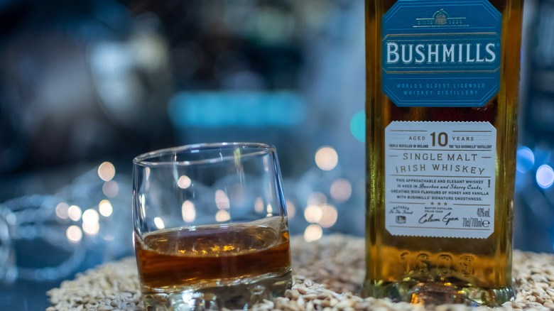 A bottle of Bushmills 10-year shown on a pile of grain next to a filled glass