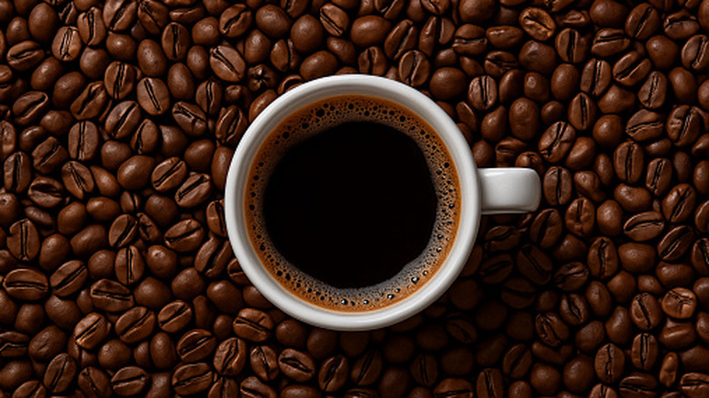 Top view of a dark cup of coffee pictured with a backdrop of whole coffee beans.