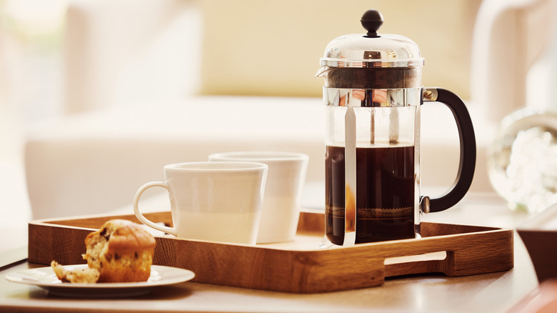 A breakfast tray setup with two white mugs, a French press, and a muffin.