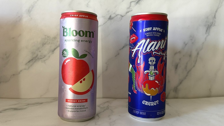 Cans of Bloom Crisp Apple and Alani Nu Ruby Apple energy drinks next to each other on marble background