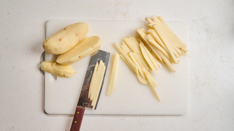 slicing potatoes into french fries on a cutting board
